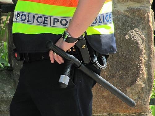Police officer wearing high-visibility vest holding tactical rifle equipment outdoors