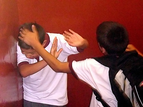 Two people engaged in physical altercation or self-defense training against red wall background