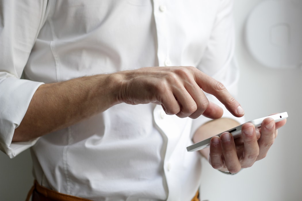 Man in white shirt holding and gesturing at smartphone screen with finger
