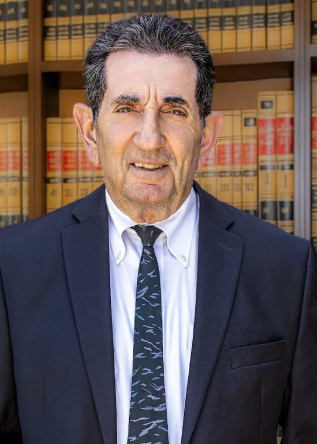 Professional headshot of mature male lawyer in navy suit and tie standing in front of law library with legal books