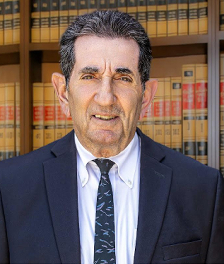 Professional headshot of a male attorney in law library with law books background, wearing dark suit and tie.