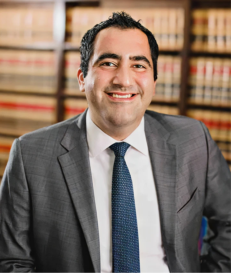 Professional portrait of man in gray suit and blue tie smiling in law library with legal books background