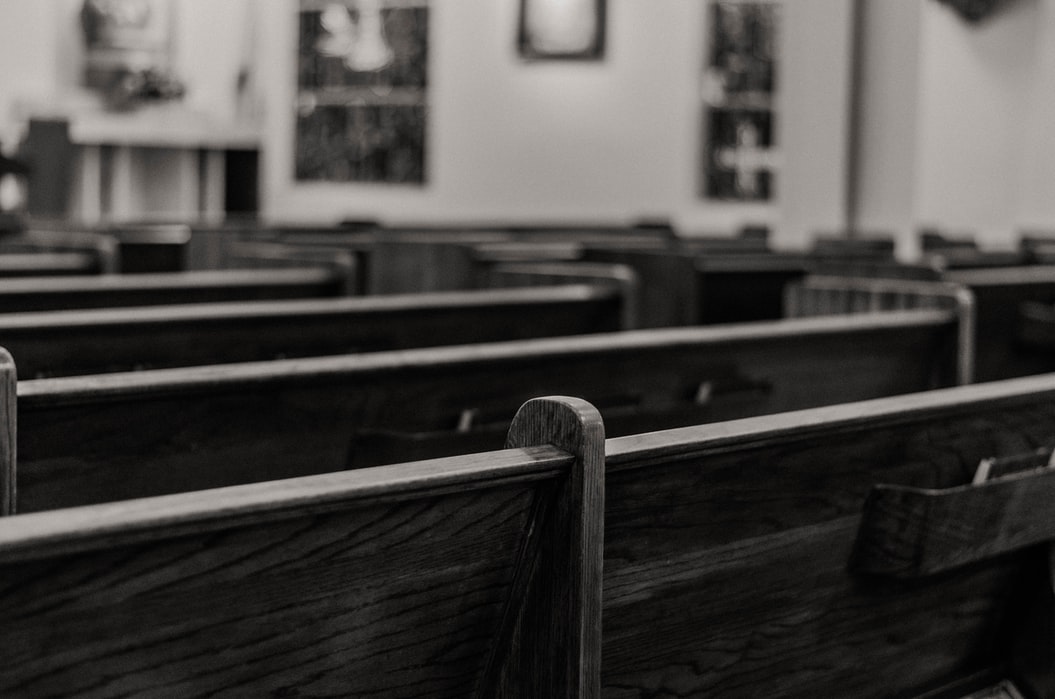 Empty church pews in black and white with wooden benches and blurred altar in background