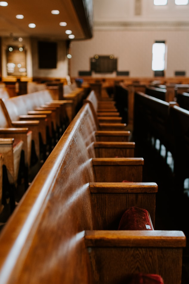 Interior of a wooden church pew with red cushions and piano in background