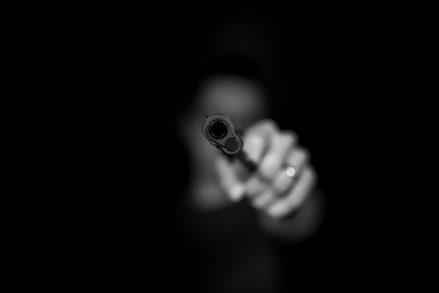Black and white image of person pointing gun directly at camera against dark background